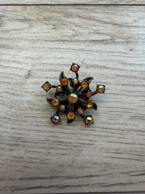 Close view of atomic flower brooch showing prong-set stones on dark metal